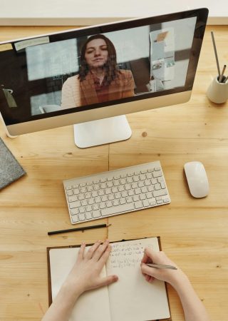 Person taking notes during a video call at a neatly organized home desk, showing remote work lifestyle.